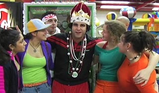 Man wearing a crown is surrounded by women in a video arcade
