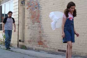 Girl wearing angel wings walking down an alley
