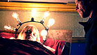 Woman with light bulb halo lies in bed while watched over by her husband