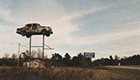 Car sitting on top of a tall tower in an abandoned field