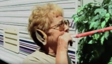 Elderly woman wearing an elf ear blowing on a party favor in a trailer park