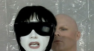 Bald man observes singing mannequin wearing sunglasses