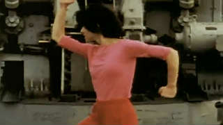 Woman in pink outfit dancing in front of heavy machinery