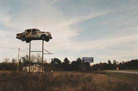 Car sits on top of a tall tower in an abandoned field