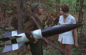 WWII soldier carrying a missile while talking to a pretty girl in a forest