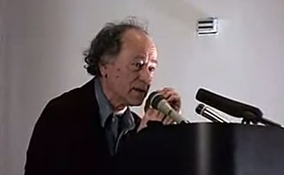 Jonas Mekas gives a lecture from a podium
