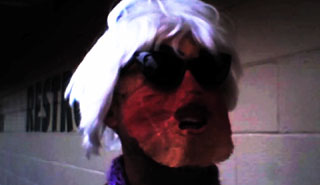 Man wearing sunglasses, a felt mask and an Andy Warhol silver wig