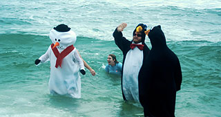 People dressed as penguins and a snowman stand in the freezing ocean