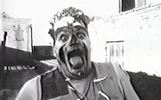 Black and white image of a man with a painted face sticking his tongue out