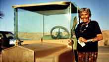 Older woman stands next to a golf cart in the desert