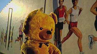 Teddy bear walks alongside a mural of joggers