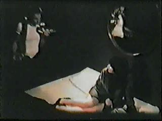 Film still from Black Box by Beth B and Scott B featuring a woman being interrogated in a dark room