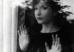 Film still from Meshes of the Afternoon featuring Maya Deren looking out a window