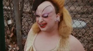 Film still from Pink Flamingos featuring Divine eating dog poop