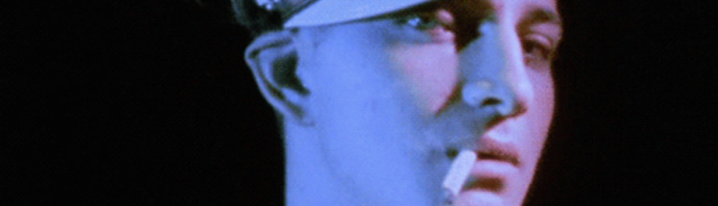 A biker smoking a cigarette gazes into the camera in a still from the Kenneth Anger film Scorpio Rising