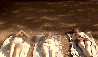 Three teenage girls lie on blankets outside on a patch of grass